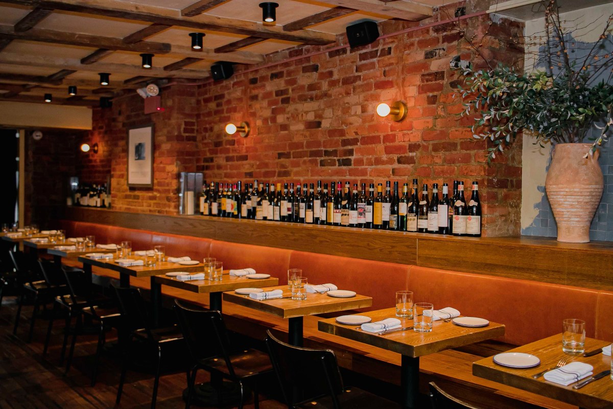 Dining room interior with brick wall, wine bottle display, and set wooden tables