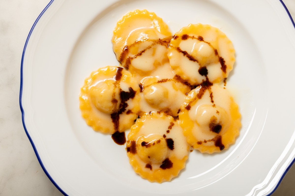 Plate of orange ravioli topped with balsamic drizzle on white scalloped plate
