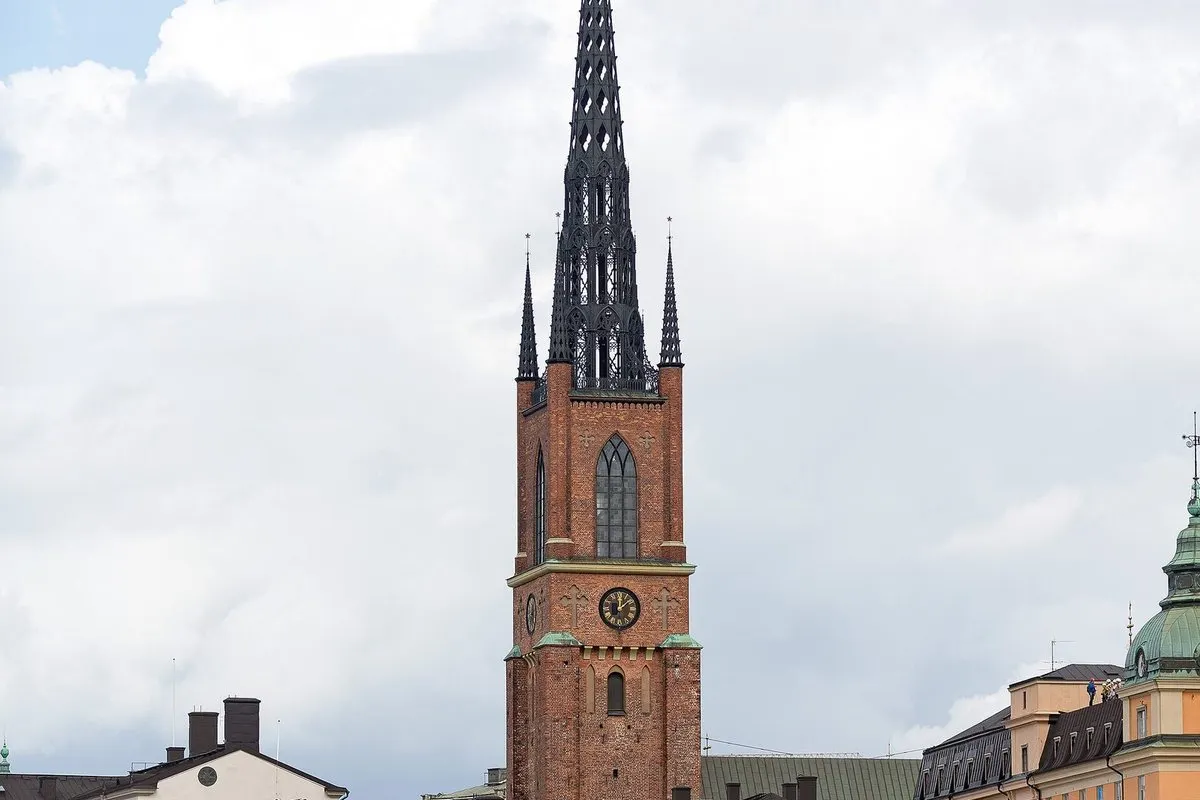The red-brick tower and openwork cast-iron spire of Riddarholmen Church in Stockholm against a cloudy sky