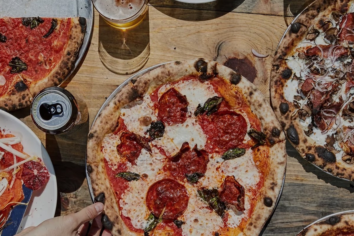 Overhead shot of a pepperoni pizza, beer, and other dishes on a wooden table at Roberta's