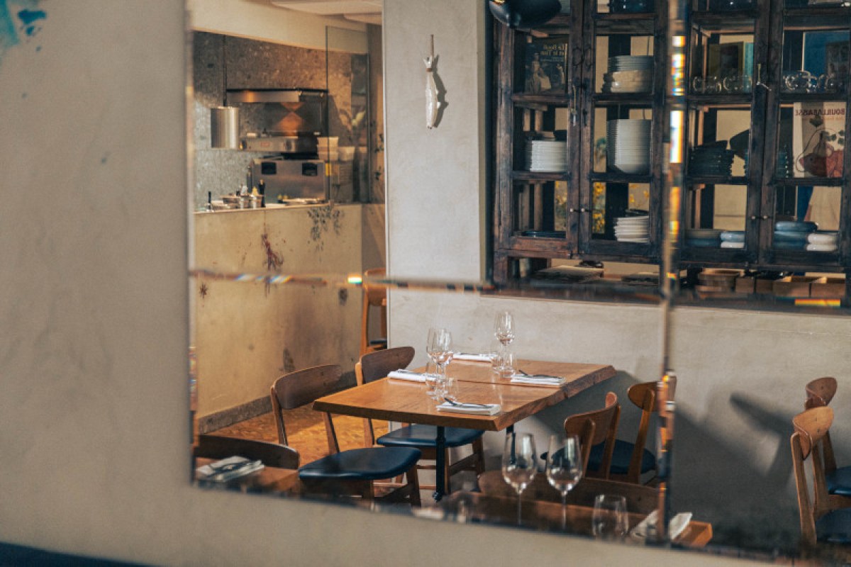 View through a window into Rooster's dining room with wooden tables, set glassware, and shelves of crockery