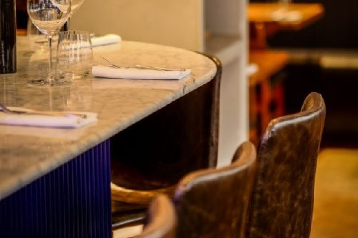 Close-up of a marble bar counter with wine glasses and leather chairs in the dining room