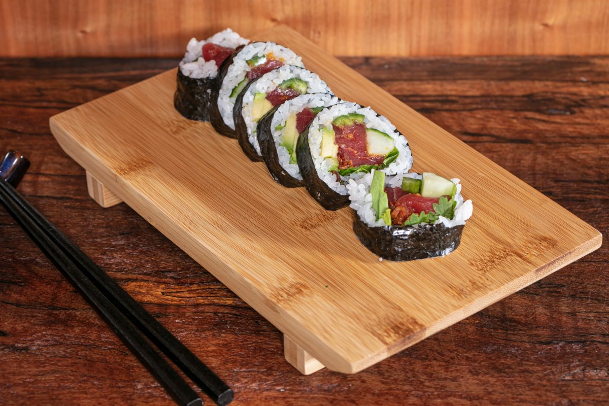 Sliced sushi roll with tuna, avocado, and cucumber on a wooden board with chopsticks