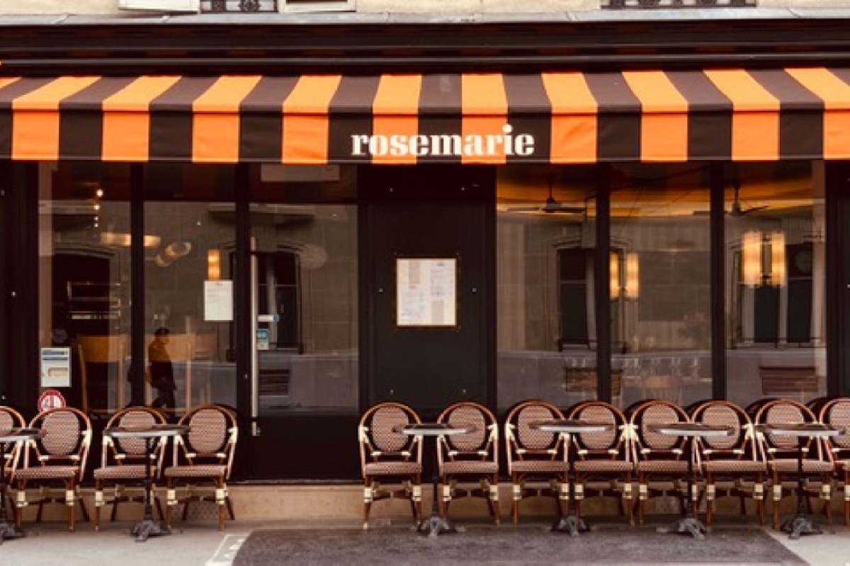 Exterior of Rosemarie restaurant with orange-striped awning, large windows, and outdoor bistro chairs and tables.