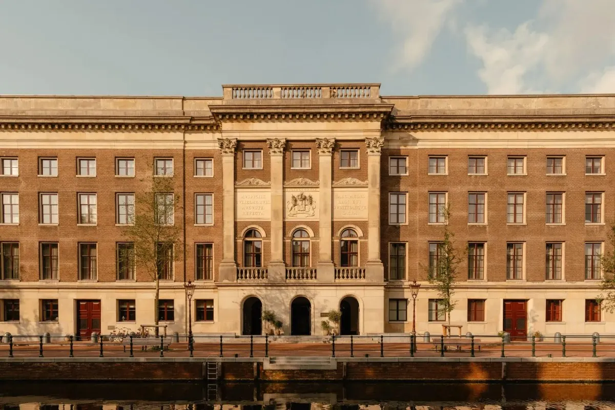 Full front facade of Rosewood Amsterdam hotel along the canal, classical brick and stone building at golden hour