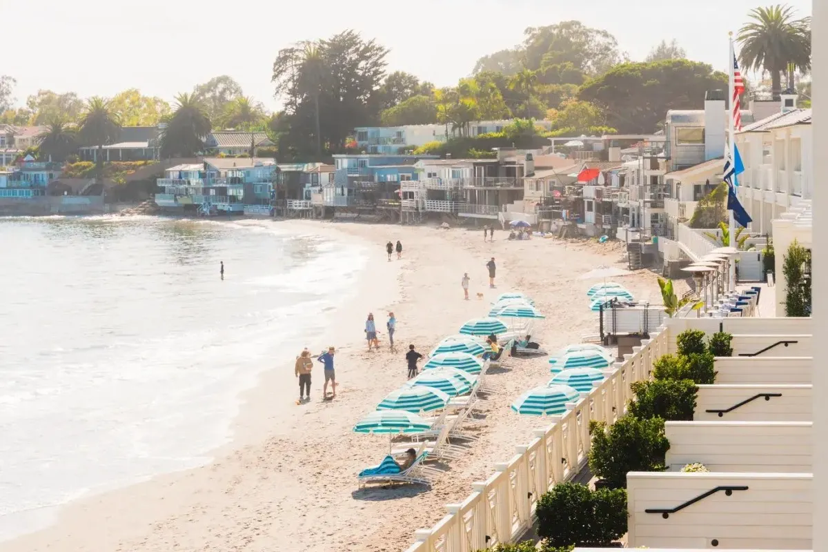 Beach view with Rosewood Miramar Beach's white building, balconies and flags, umbrellas lining the shore