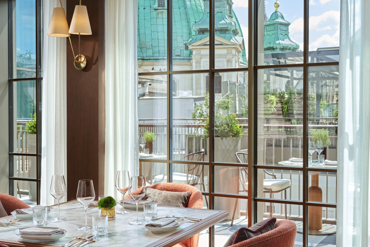 Hotel restaurant with marble table set for dining, floor-to-ceiling windows showing green domed rooftops of Vienna
