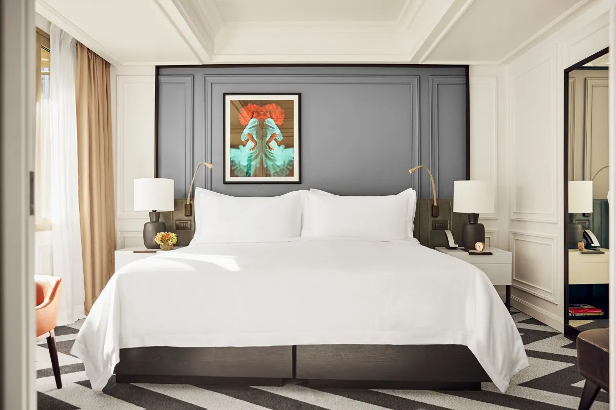 Elegant bedroom with a large white bed, gray paneled headboard, and modern artwork