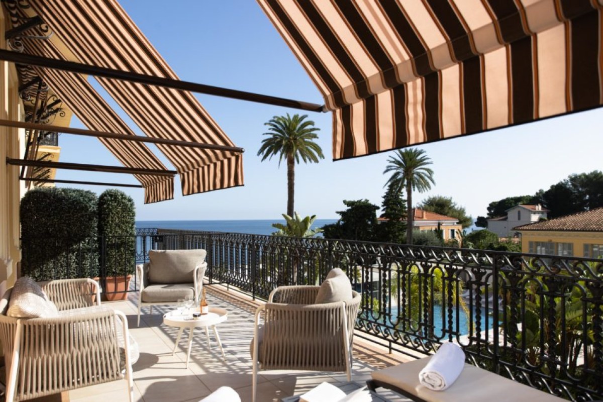 Private terrace with striped awning, lounge chairs, and sea view overlooking palm trees and the pool below