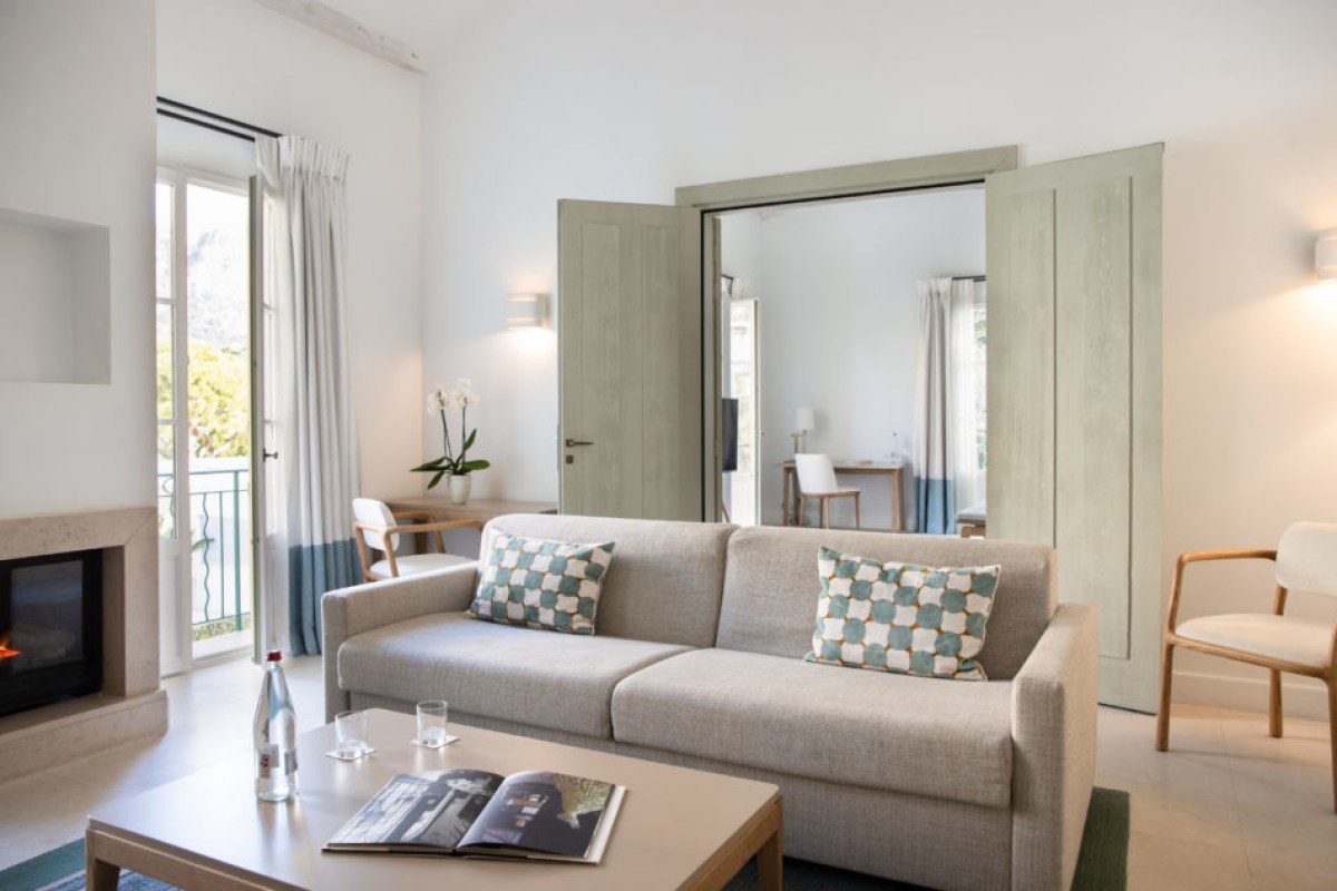 Bright suite living room with gray sofa, fireplace, and doors opening to a balcony