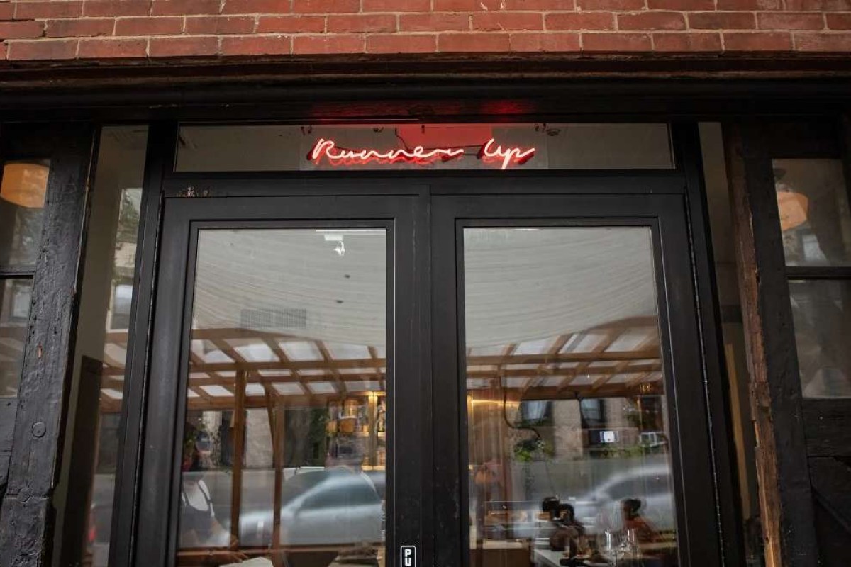 Restaurant entrance with red neon 'Runner Up' sign above black-framed glass doors in brick facade.