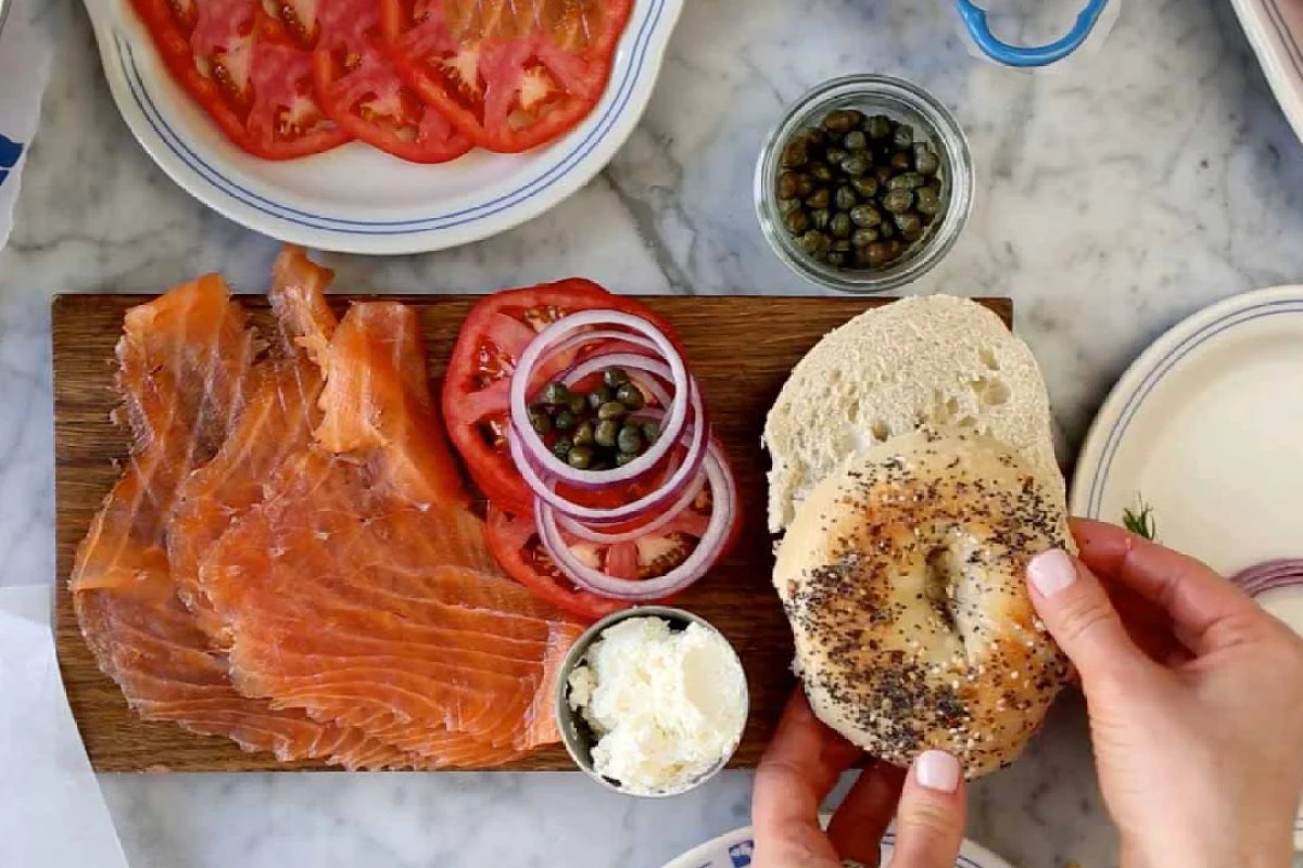Overhead view of bagel with lox, cream cheese, tomato, onion and capers on wooden board