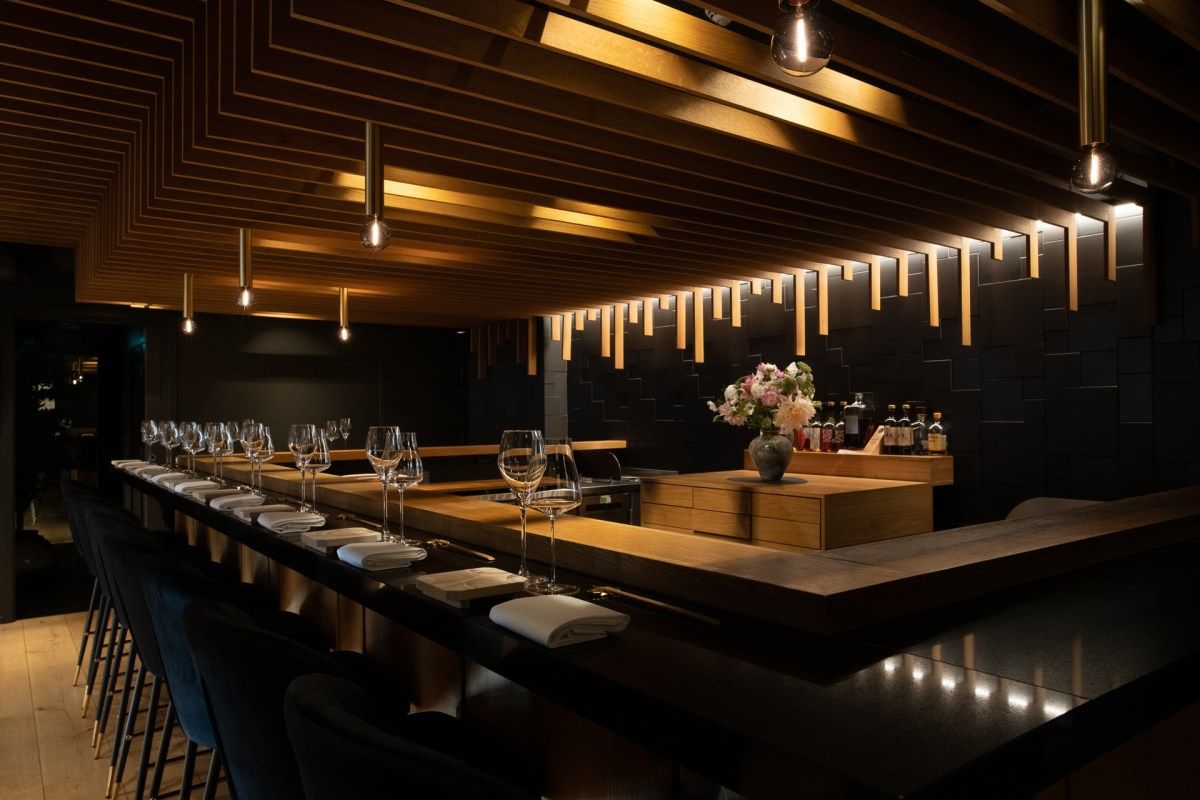 Sleek sushi bar counter with wine glasses, folded napkins, and a flower arrangement in Sabi Omakase Oslo's dining room.