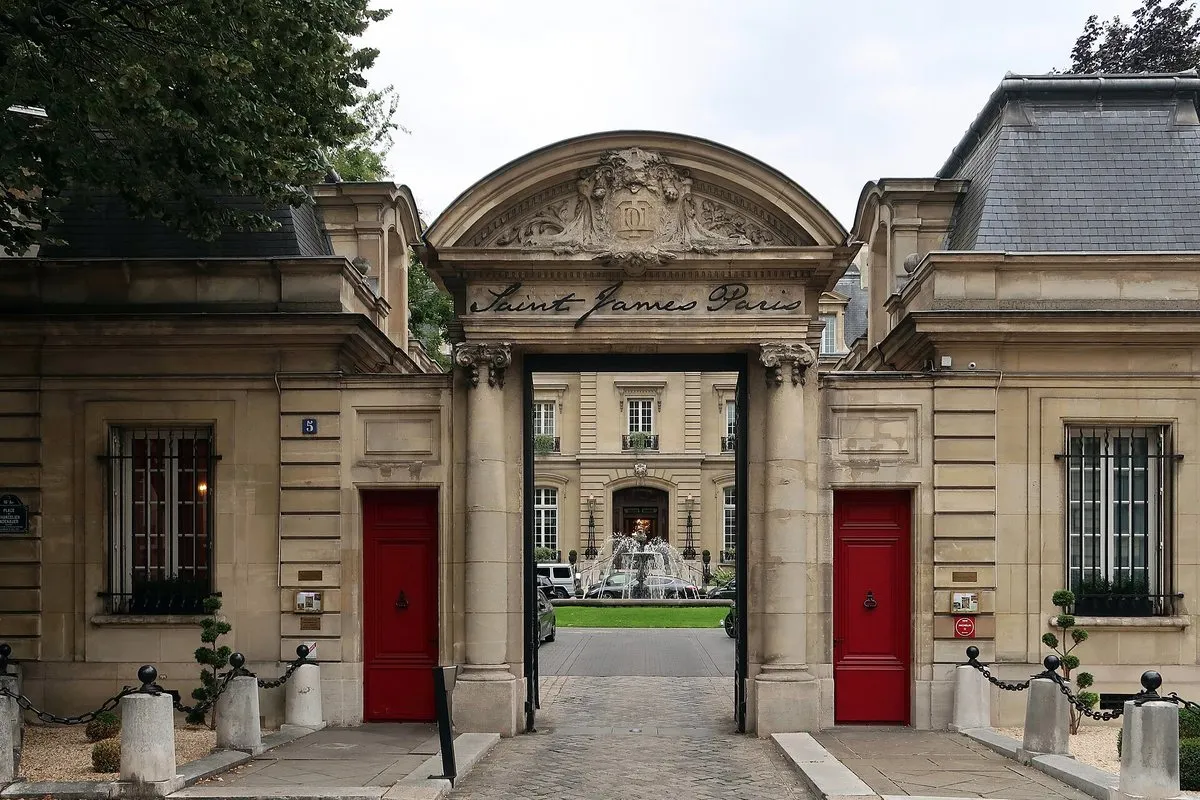 The gatehouse of Saint James Paris with red doors and a view through the arch to the fountain and the mansion