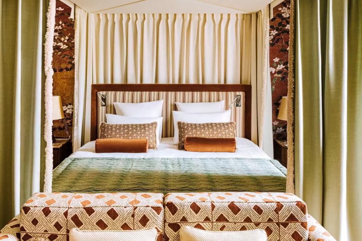 Four-poster bed with green curtains, striped headboard and floral wallpaper in a guest suite