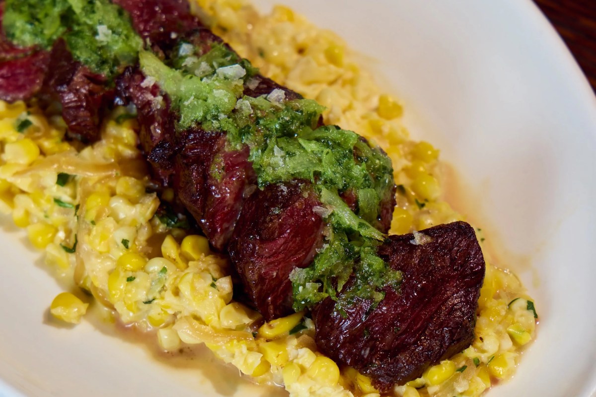 Grilled steak slices topped with herb sauce over creamed corn on a white plate