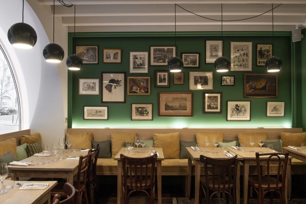 Dining room with green gallery wall, dark pendant lamps, and mustard-cushioned banquette seating at wooden tables