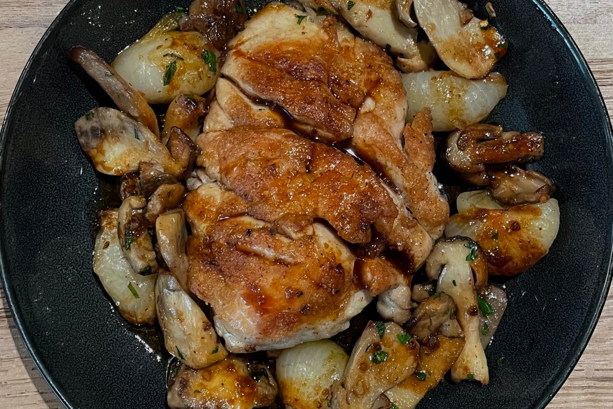 Overhead shot of roasted chicken with mushrooms and small onions on a black plate