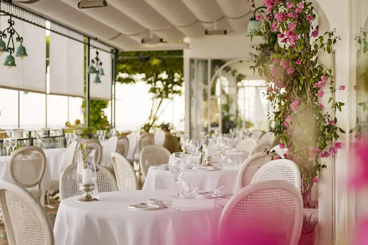 Elegant terrace restaurant with white-clothed tables, cane chairs, and pink bougainvillea