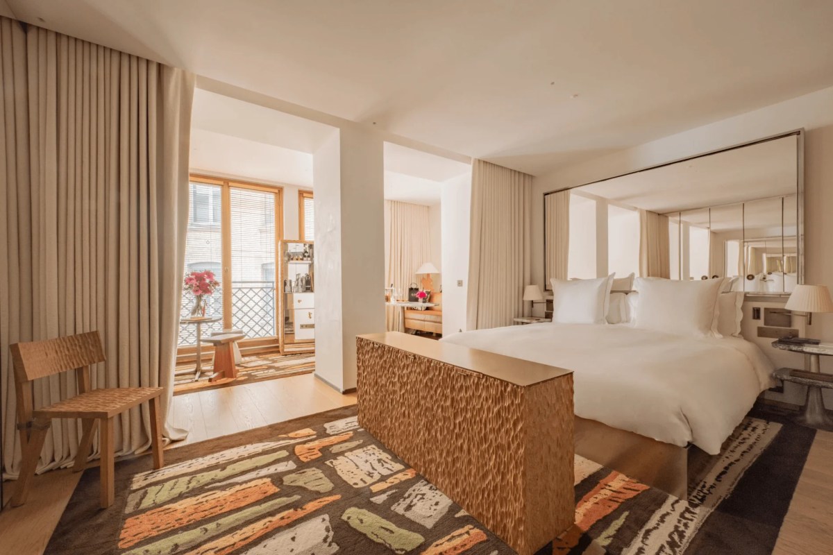 Spacious hotel suite with king bed, mirrored headboard, patterned rug, and balcony with city view