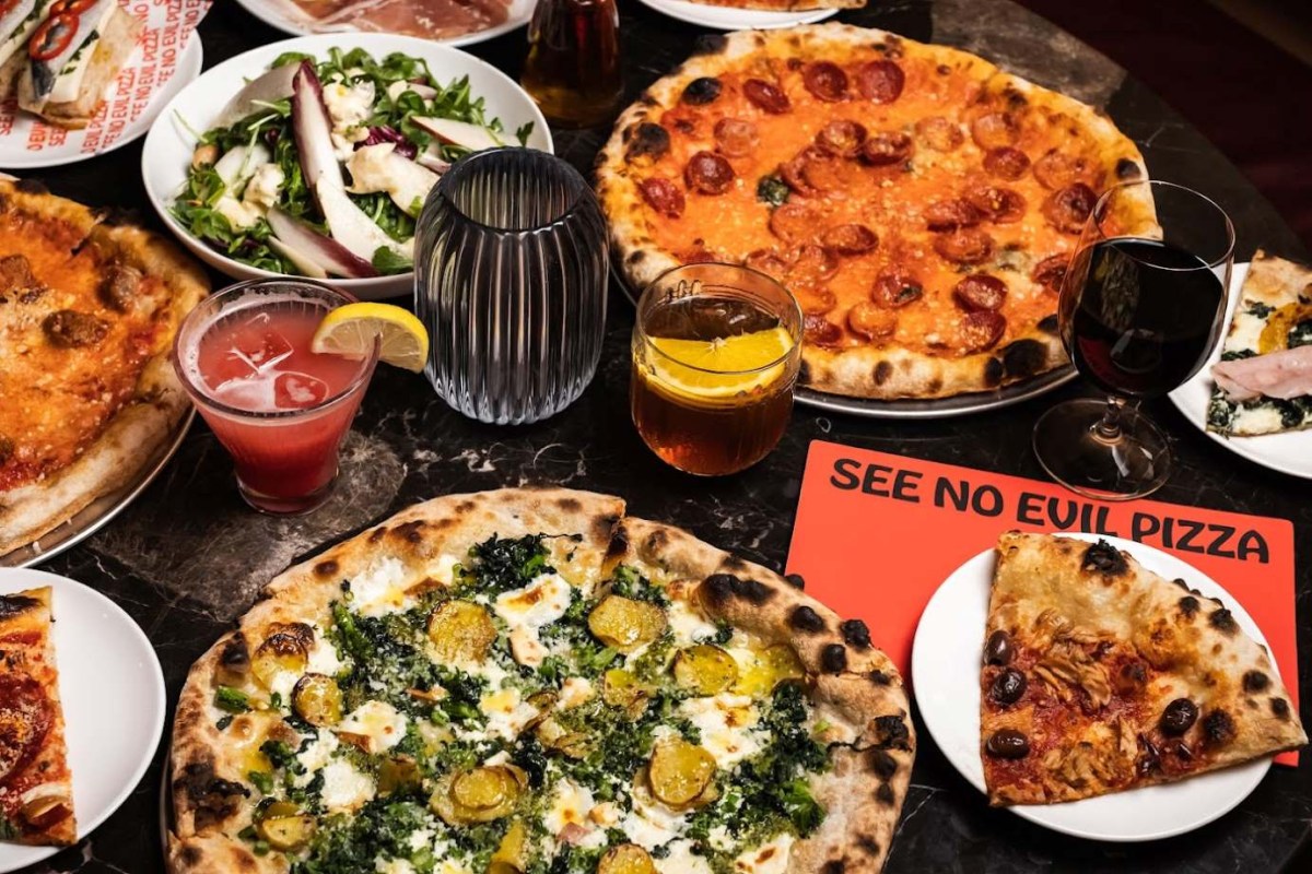 Table spread with multiple pizzas, salad, cocktails, wine, and a See No Evil Pizza menu card