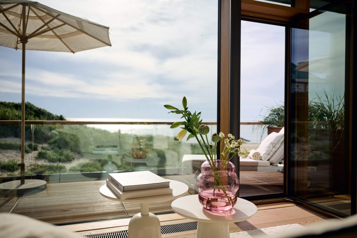 Guest room terrace with glass balustrade, umbrella, side tables with books and flowers, dune and sea view