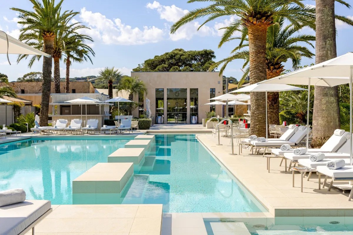 Pool area with loungers, umbrellas and hotel building facade behind
