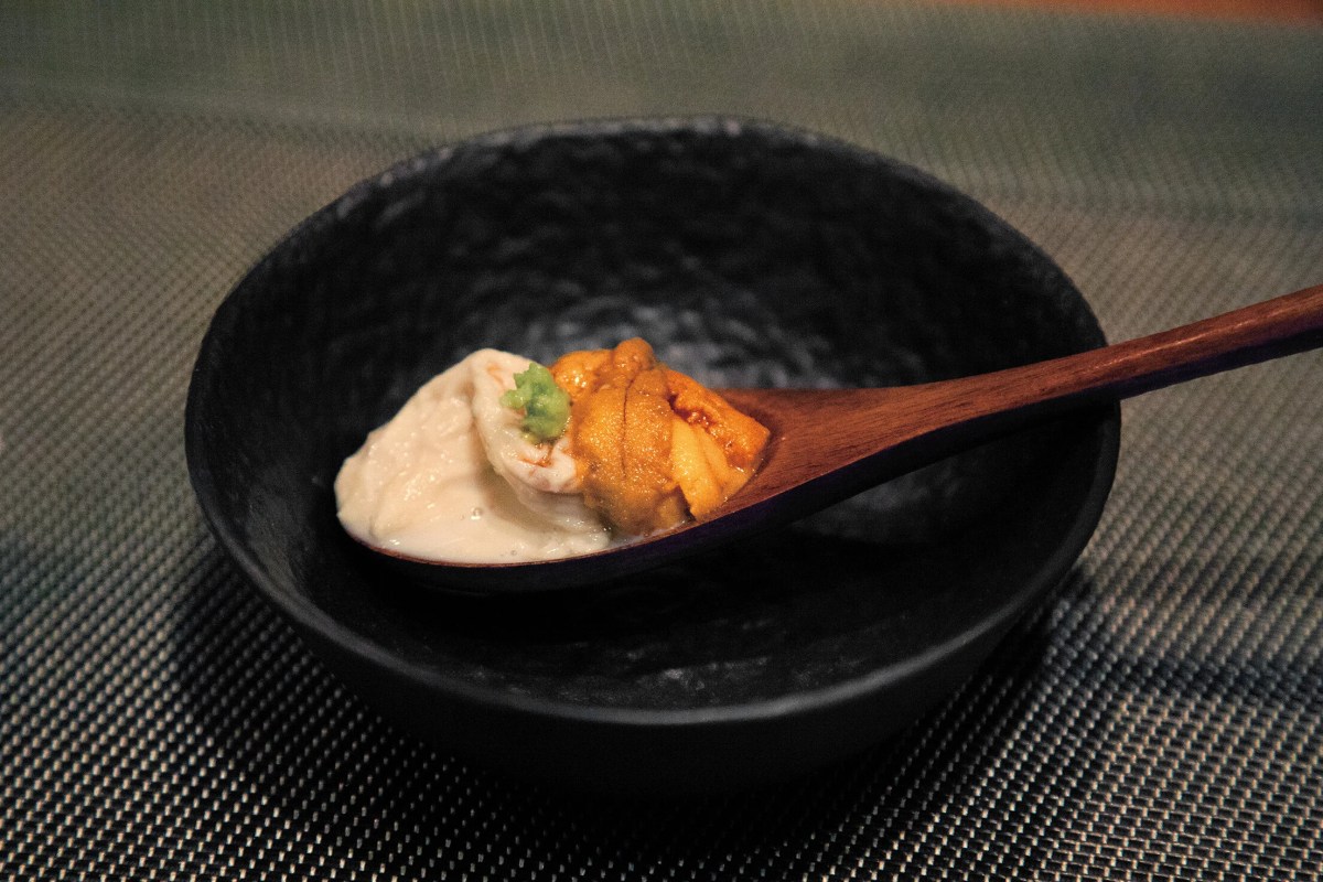 Wooden spoon holding a dollop of uni and tofu with a touch of wasabi in a black textured bowl
