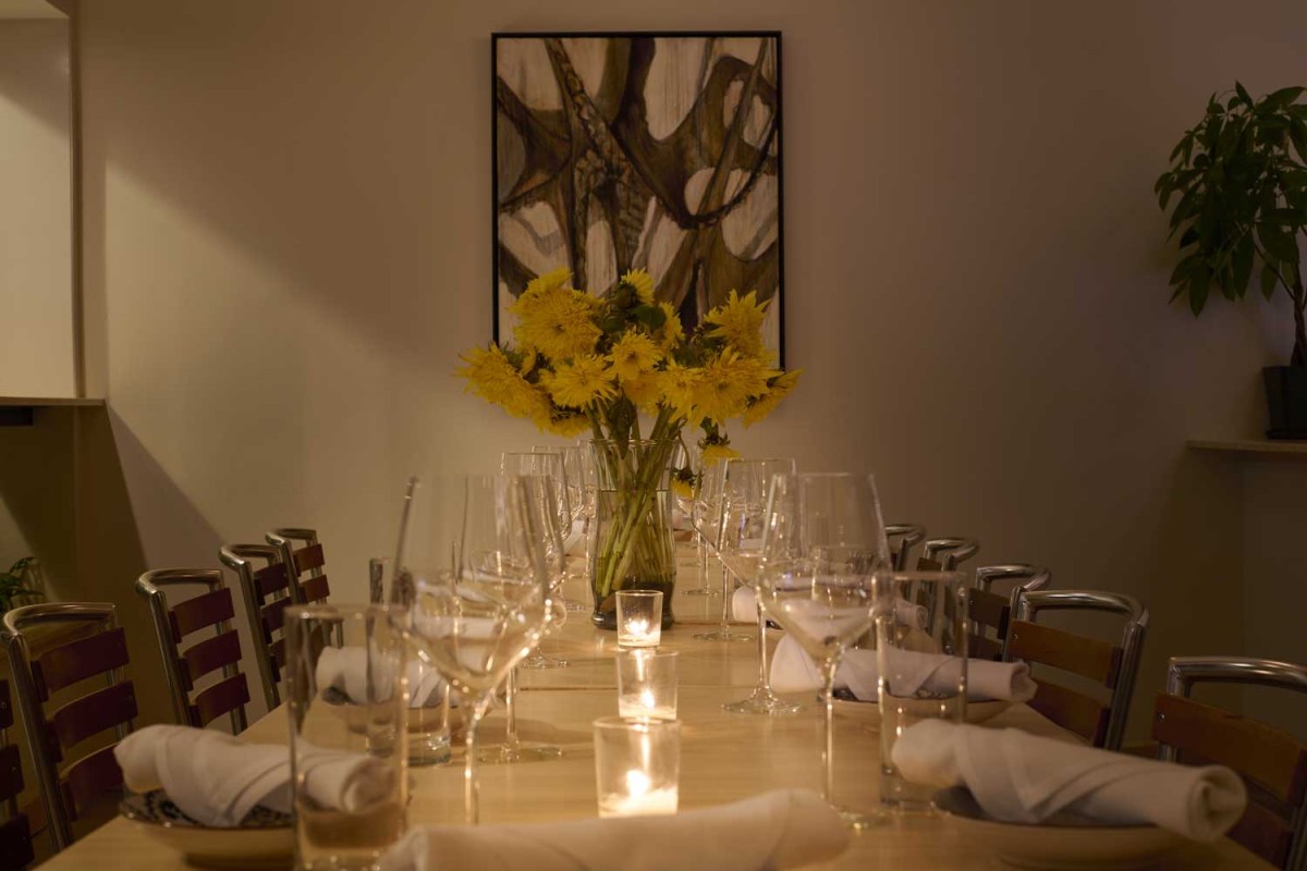 Dining room interior with long table set with wine glasses, candles, napkins and a yellow flower centerpiece