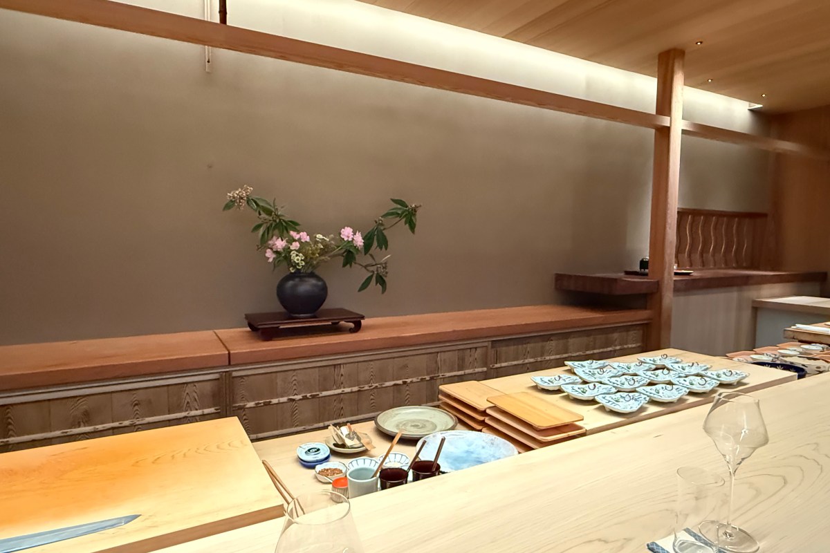 Interior sushi counter at Shingo with wooden bar, ikebana flower arrangement, and small dishes laid out