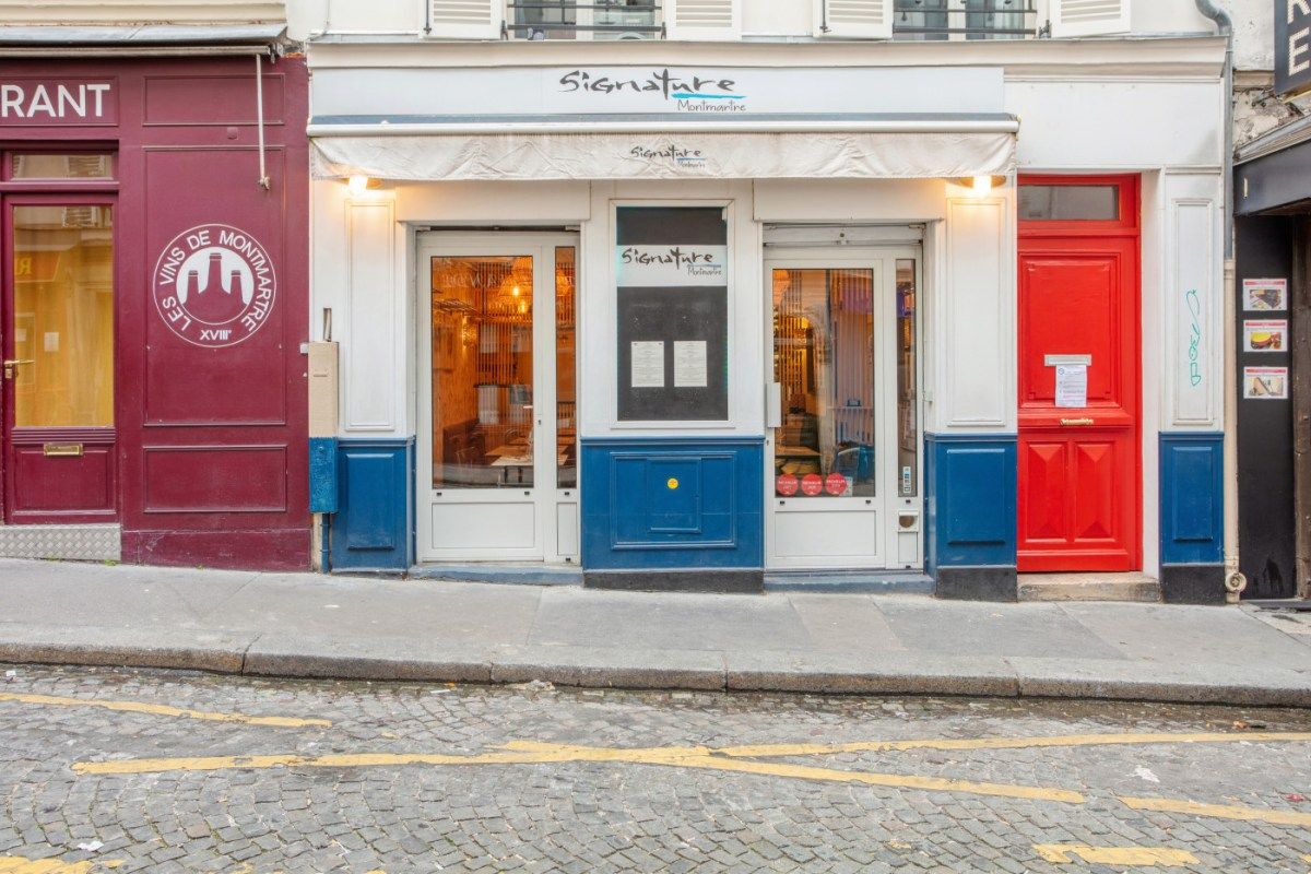 Exterior storefront of Signature Montmartre restaurant with blue and white facade and red door of neighboring building