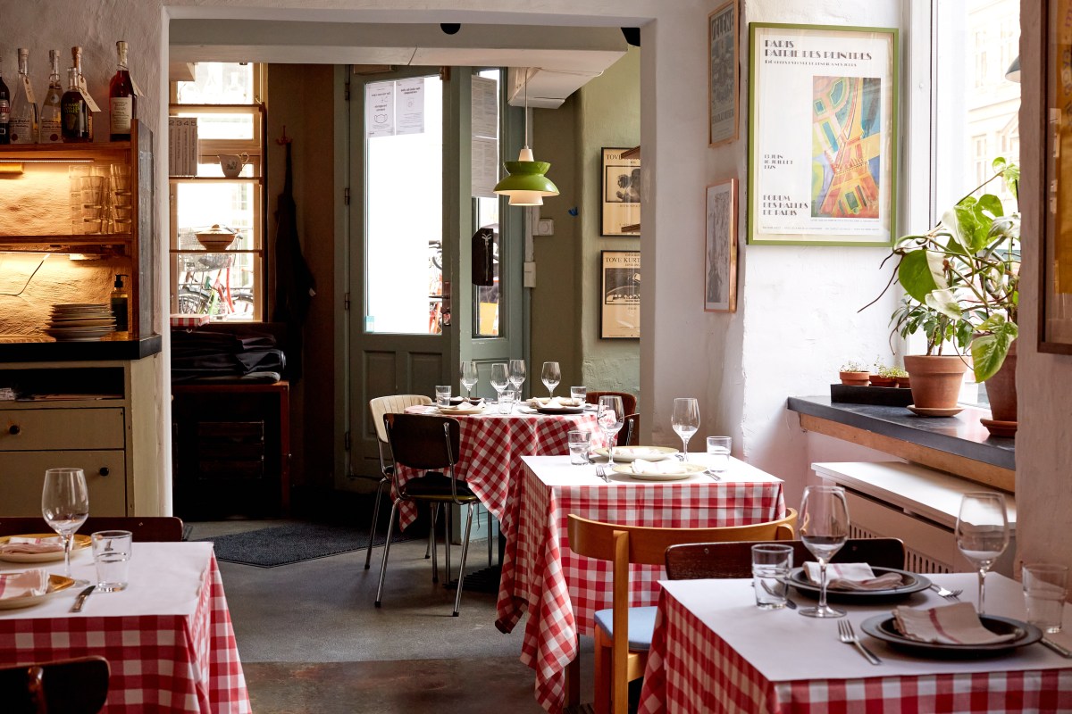 Cozy dining room at Silberbauers Bistro with red-checkered tablecloths, wine glasses, framed art posters, and a view through a doorway to another seating area.