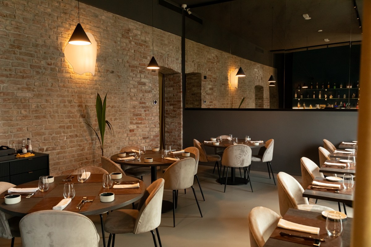 Dining room with exposed brick walls, round tables set with glassware, and bar visible through mirror