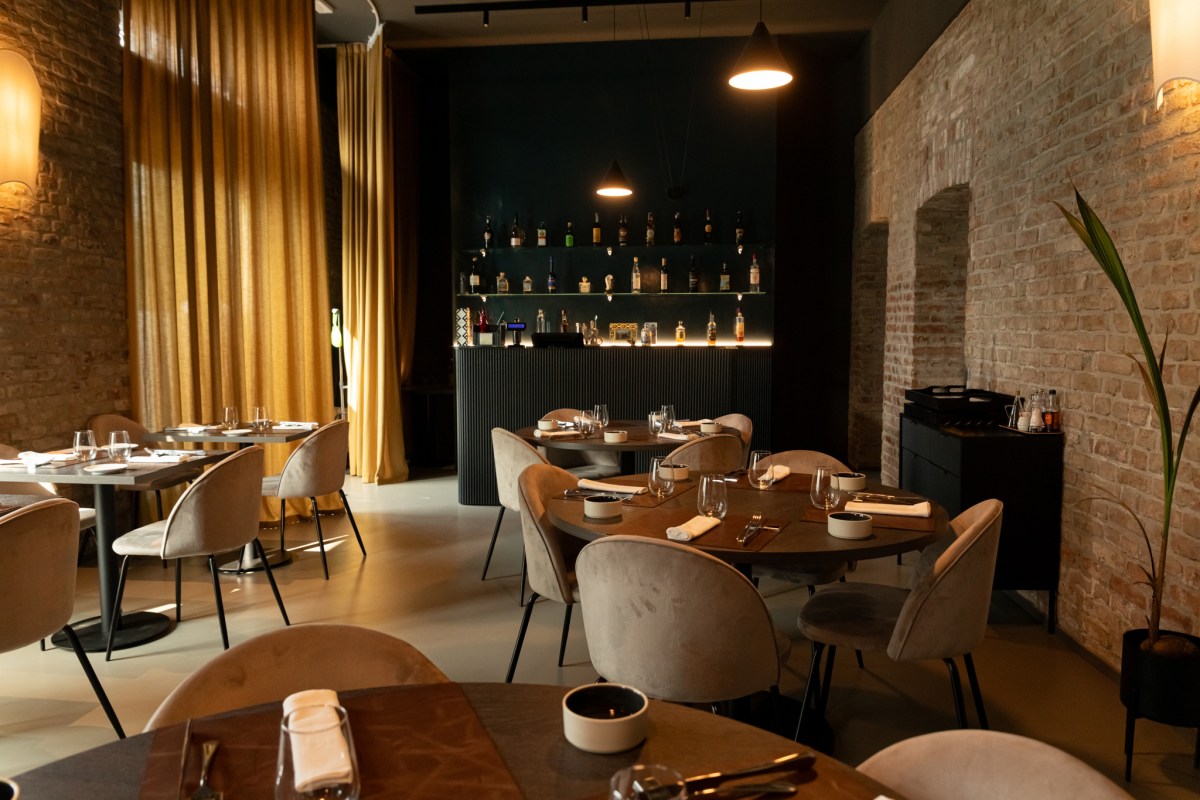 Restaurant interior with brick walls, set tables, pendant lights, and a bar with bottles in the background