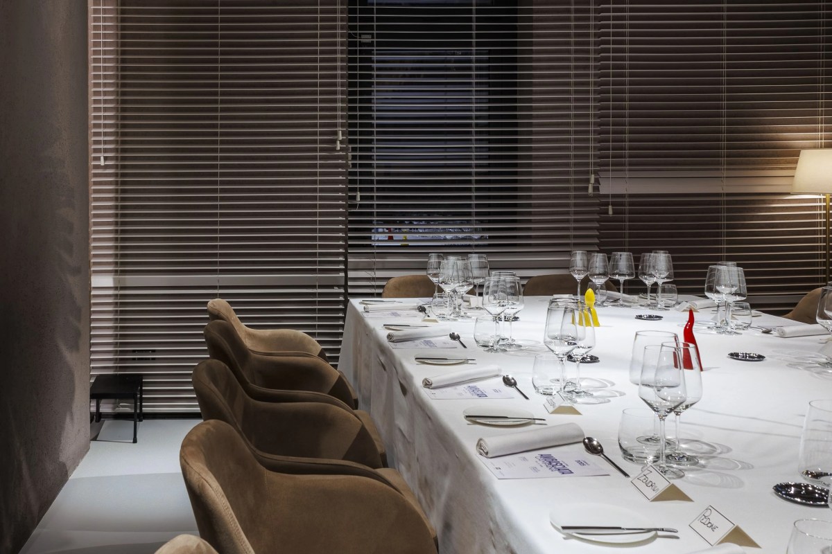 Long dining table set with wine glasses and name cards in front of window blinds