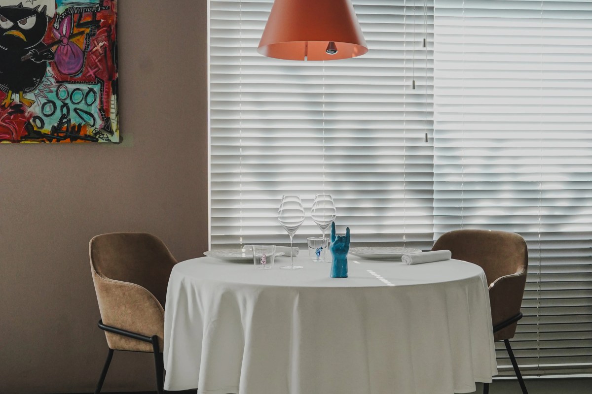 Round table set for two with wine glasses beside a window with blinds