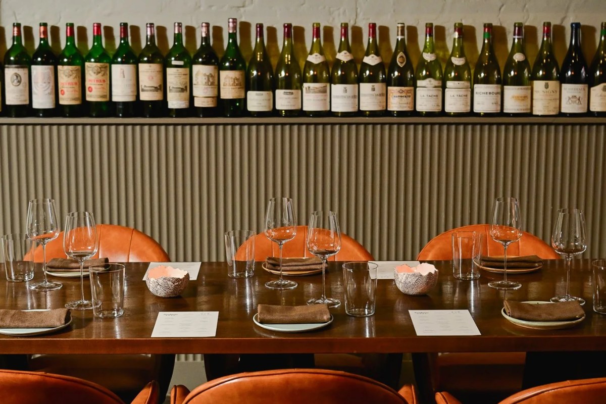 Private dining table set with wine glasses, napkins, and a wall of wine bottles behind