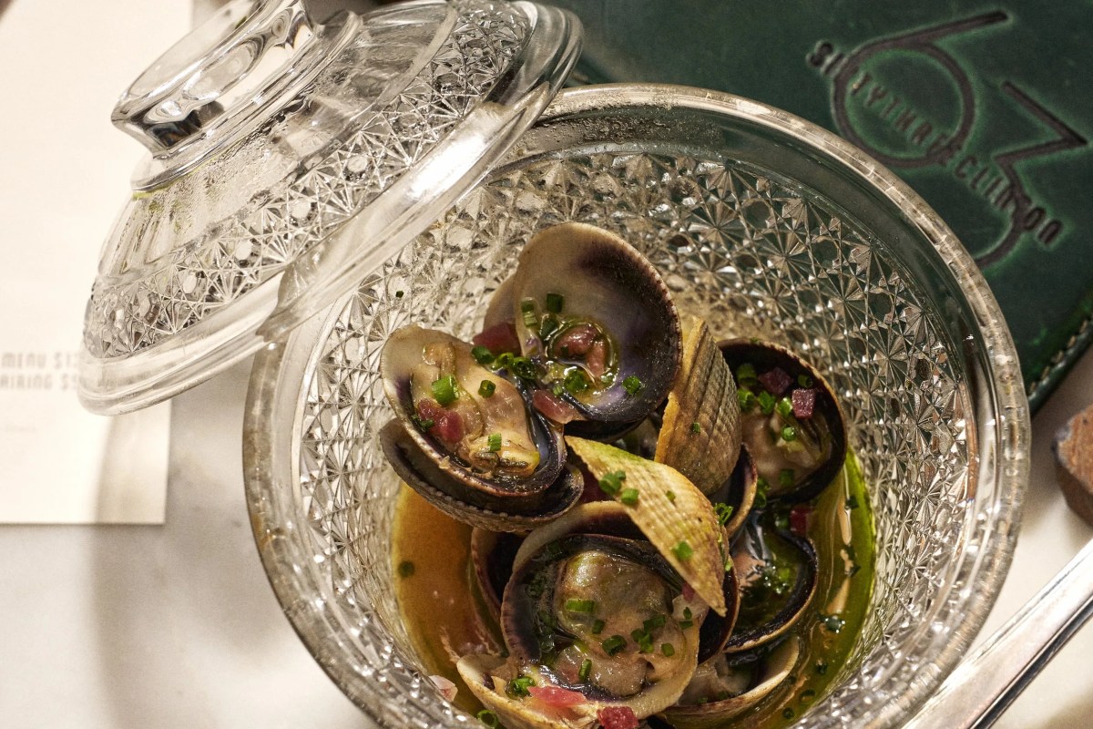Overhead view of clams in broth in a cut-glass bowl with lid, restaurant menu visible