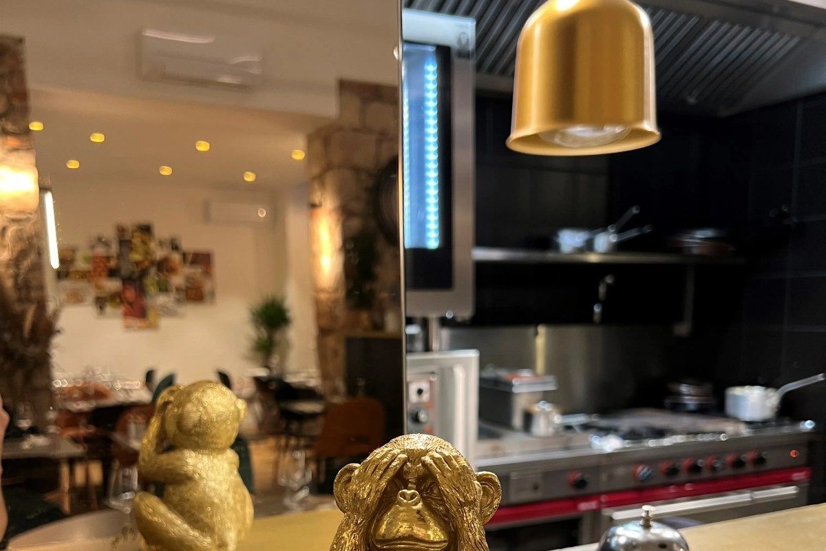 Reflection showing dining room tables and professional kitchen, with gold decorative monkey figurines in foreground