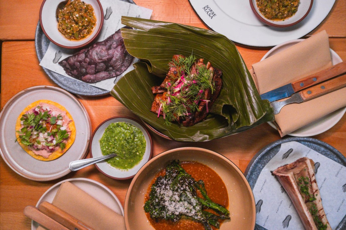Overhead view of a spread of dishes on a wooden table at Sobre Masa, including tacos, salsas, grilled meat and short rib