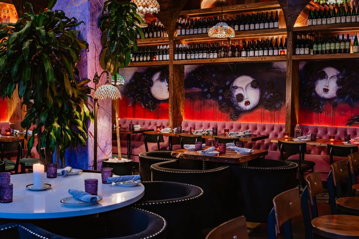 Dining room with tufted pink banquettes, wine shelves, plants and whimsical face mural