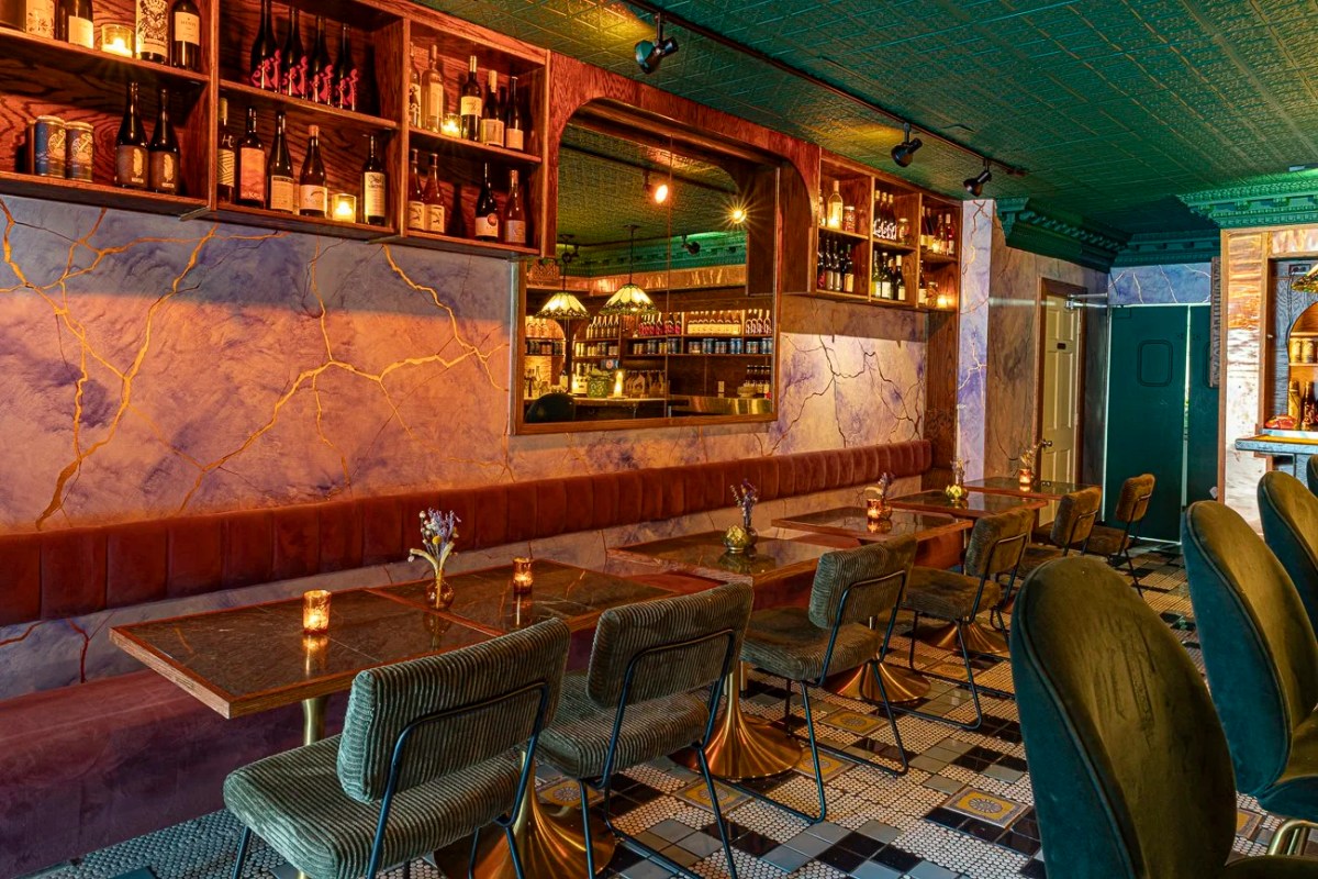 Moody restaurant bar area with marble walls, wine shelves, velvet chairs and mirrored bar back