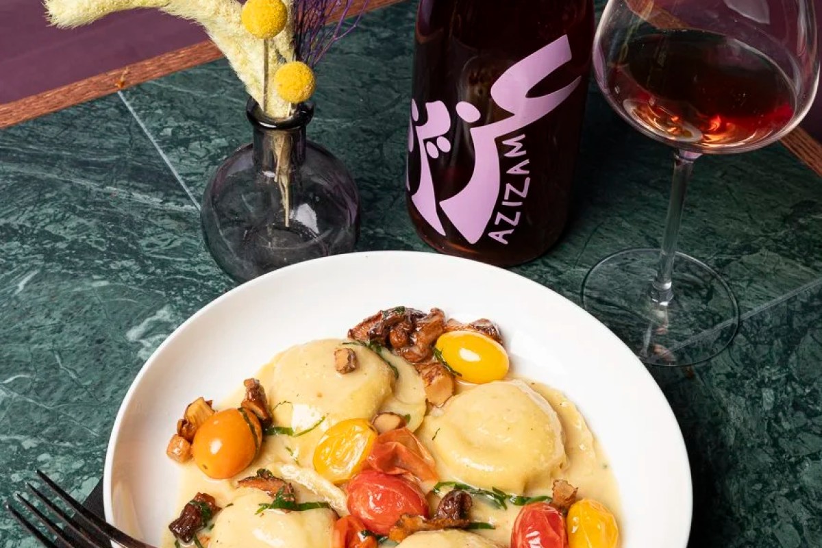 Plated ravioli dish with cherry tomatoes and mushrooms beside a glass and bottle of rosé wine