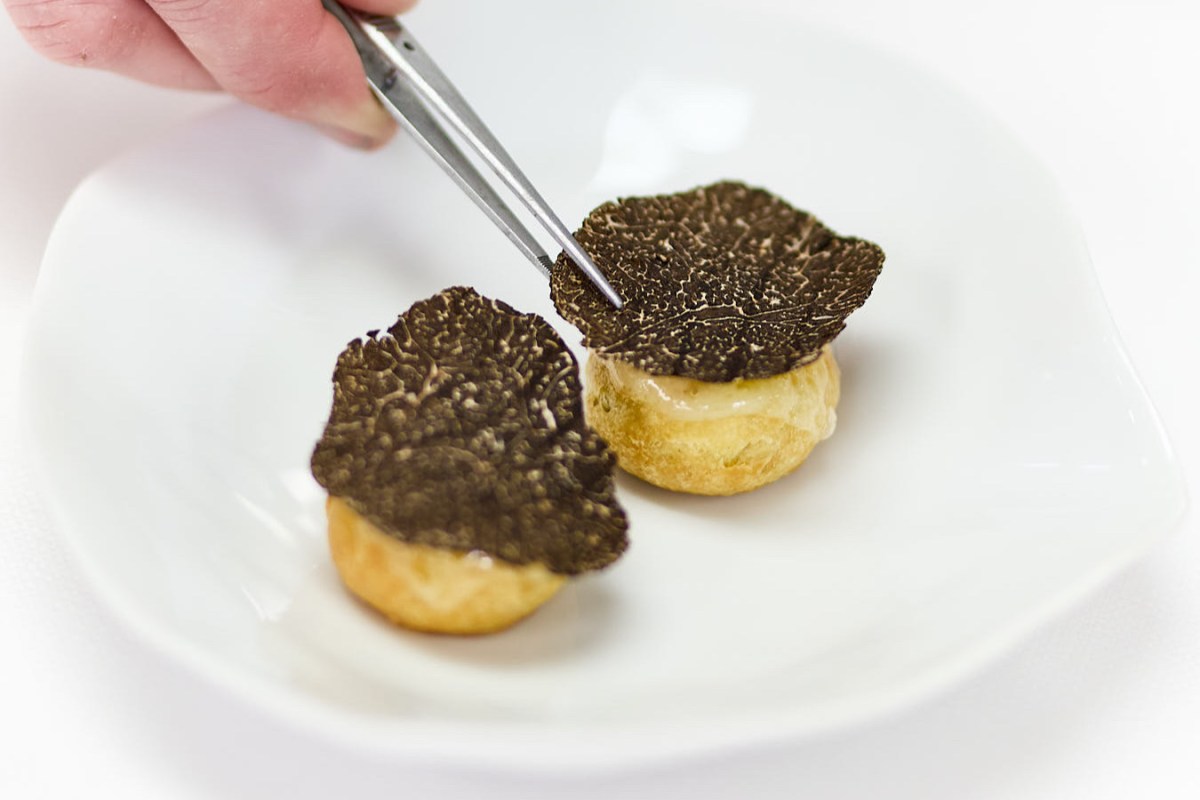 Close-up of a chef's hands placing black truffle slices onto cream puffs on a white plate