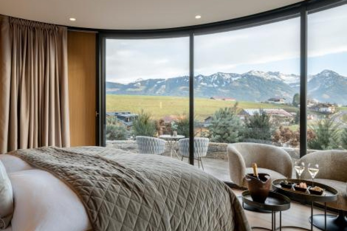 Curved-window bedroom suite with champagne service, plush bed and alpine mountain view