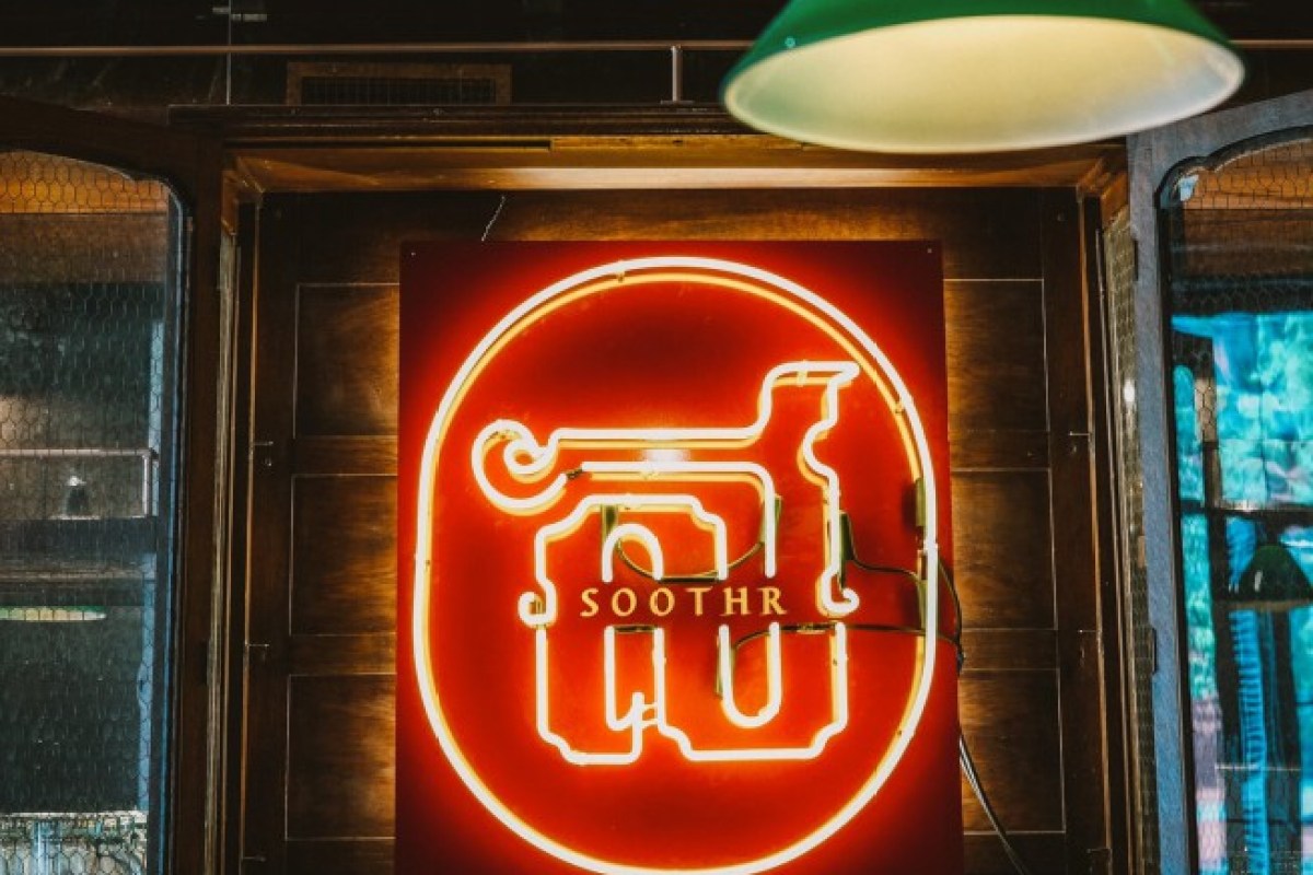 Close-up of illuminated red neon Soothr logo sign mounted on wood paneling near bar entrance