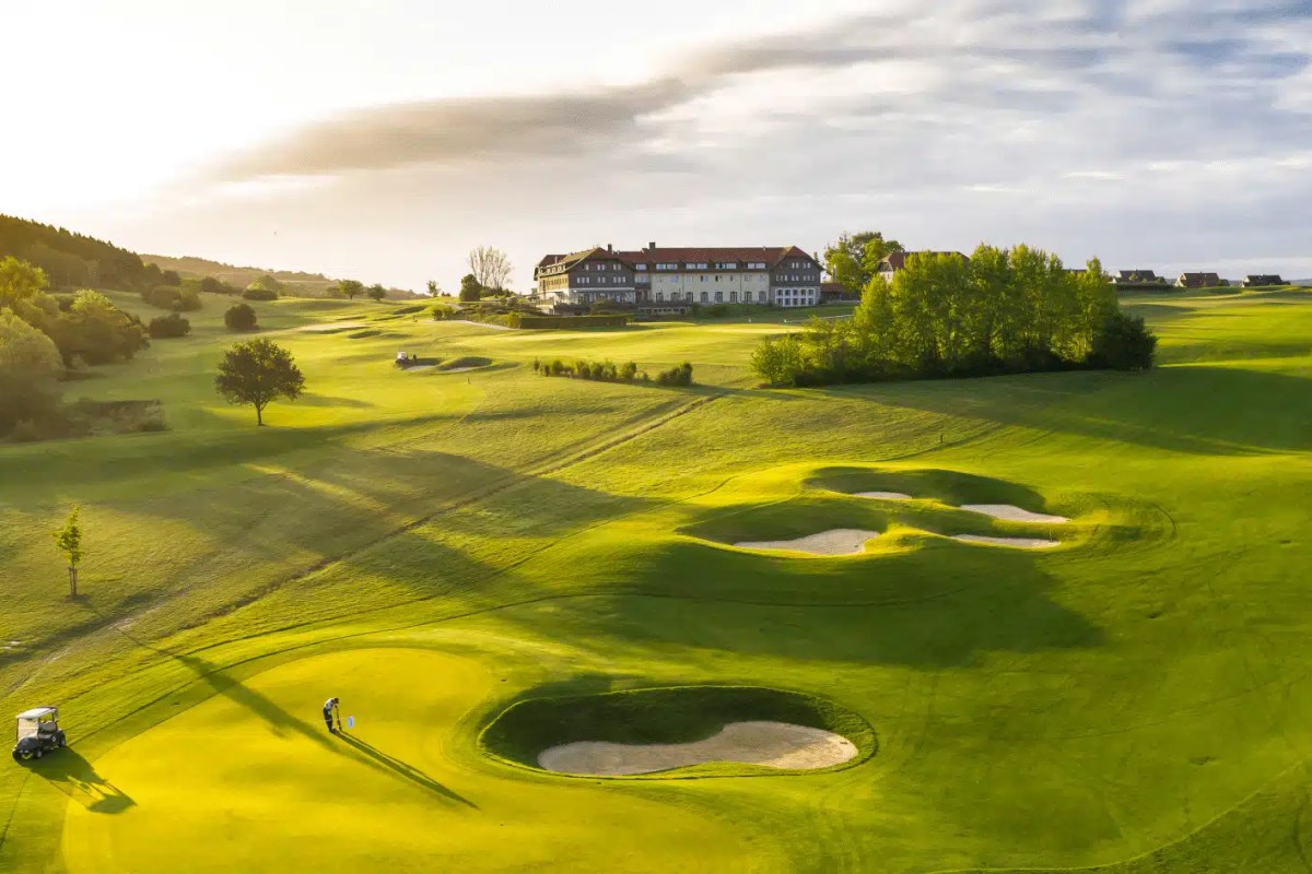 Aerial view of the hotel's white building overlooking the green golf course with sand bunkers at sunset