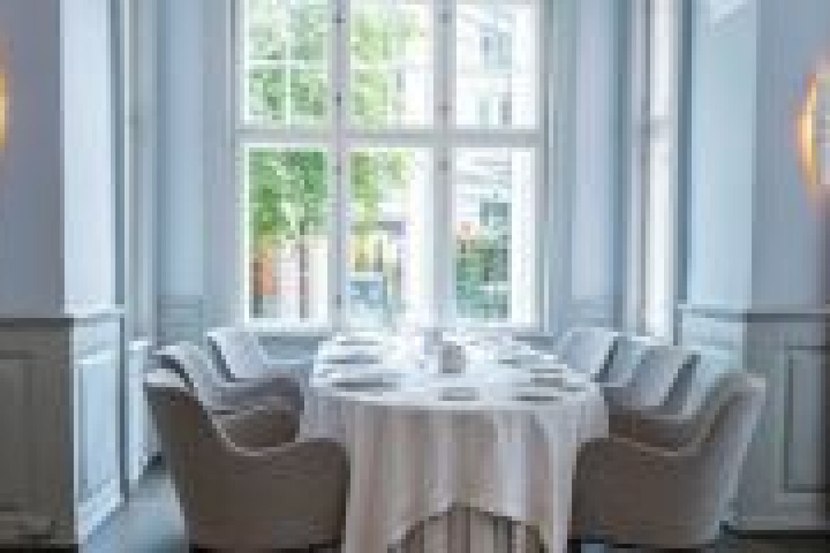 Round table set for dinner by a tall window with upholstered chairs
