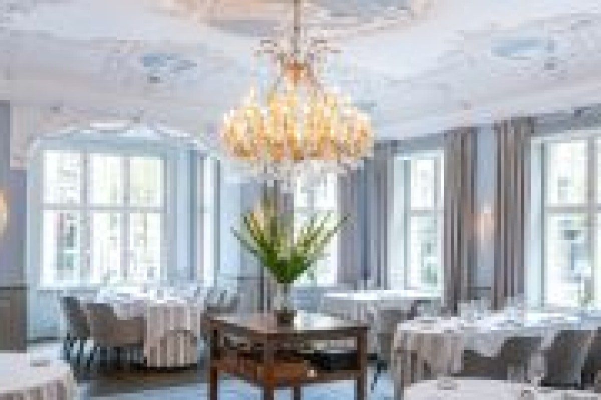 Elegant dining room with ornate ceiling, crystal chandelier, set tables and tall windows