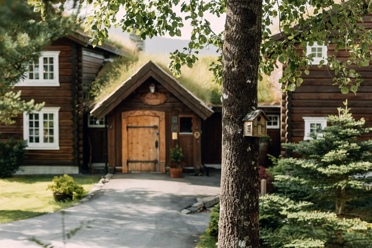 Traditional Norwegian log building with turf roof and wooden door, framed by trees and a small birdhouse